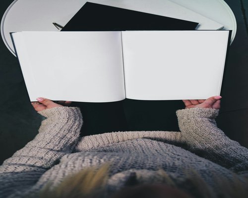 Person peacefully reading a paper book near a soft desk lamp with no screens nearby